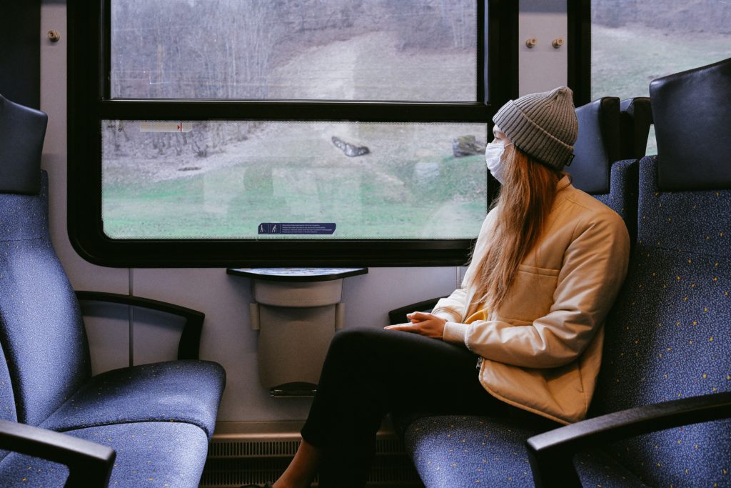 a woman wearing a mask, sitting on a train and looking out the window